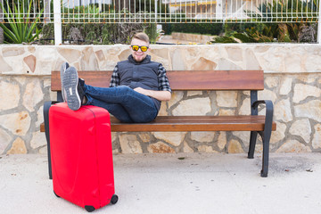 Travelling, people and holiday concept - young man sitting with suitcase. He is ready to trip