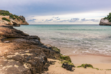 Wellen brechen sich weiß schäumend am sandig, felsigen Strand auf Mallorca