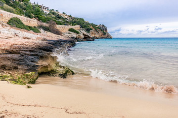 Wellen brechen sich weiß schäumend am sandig, felsigen Strand auf Mallorca