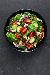 Spinach salad with fresh cucumbers, tomato, onion, pomegranate, sesame seeds and cashew nuts on...