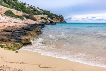 Wellen brechen sich weiß schäumend am sandig, felsigen Strand auf Mallorca