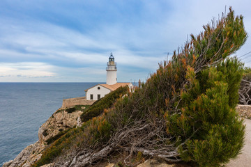 Fototapeta na wymiar Am Ende des Felsens ragt ein Leuchtturm mit Blick auf das blaue Meer