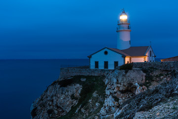 Fototapeta na wymiar Leuchtturm auf einem Felsen umringt vom Meer, zur blauen Stunde