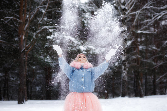 smilling young woman thowing snow in the air at sunny winter day.
