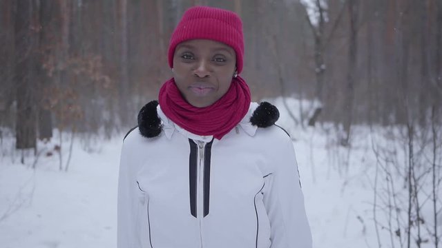 African american girl running through winter forest. Beautiful girl in warm jacket turns and looks in camera, smiling. Concept of outdoor recreation. Slow motion shooting