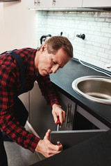 Serious master. Seniour handyman repairing kitchen cabinet