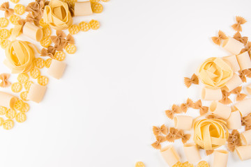 An overhead photo of different types of pasta, including spaghetti, penne, fusilli, and others, flay lay on a white background with a place for text