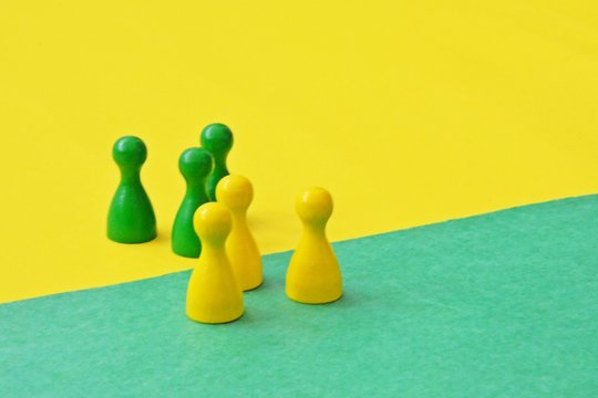 A red and a blue team of wooden game characters of a board game face each other and are greeted by the respective oppositely colored background - concept of boundaries and differences