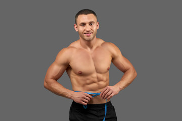 Fototapeta premium Sexy bodybuilder holding measure tape round waist.