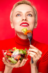Beautiful caucasian woman eating salad over red background