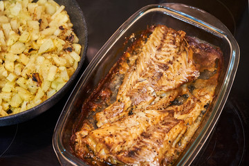 Baked fish in a plate and potatoes in a frying pan