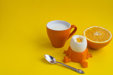 Children's breakfast: boiled egg, milk and orange on the yellow  background.Copy space.