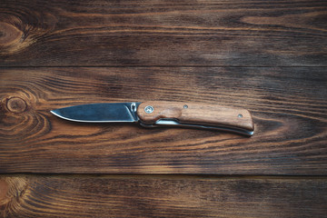 hunting bowie knife with a wooden handle on dark wooden background. Steel arms weapon. top view