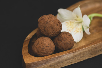 brutal and stylish handmade round chocolates on a wooden plate with a flower on a black background. close up.