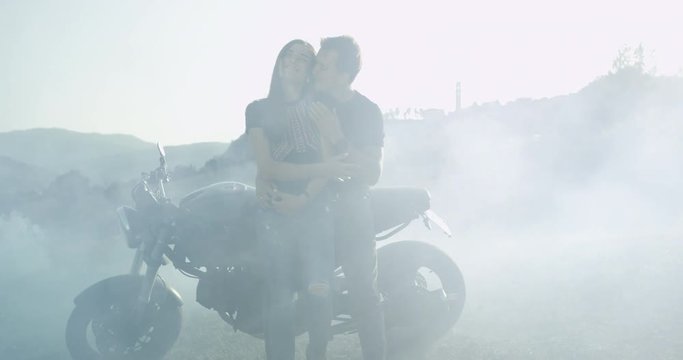 Young couple in the middle of field sitting beside of their motorcycle and enjoying the time together romantic touching each other , in blurred images