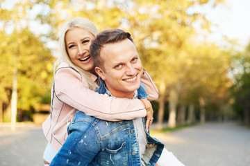 Fototapeta premium Happy couple on vacation. Lovers are laughing. Happy guy and girl. Lovers enjoy each other in the sunny park. Boyfriend carrying his girlfriend on piggyback