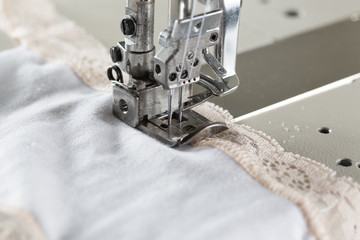 sewing process on sewing professional manufacturing machine with metal needle detailed by white caucasian woman's hands holding lace fabric for lingerie production