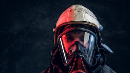 Brutal fireman in gas mask and helmet looks into camera on black background in studio