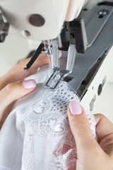 sewing process on sewing professional manufacturing machine with metal needle detailed by white caucasian woman's hands holding lace fabric for lingerie production