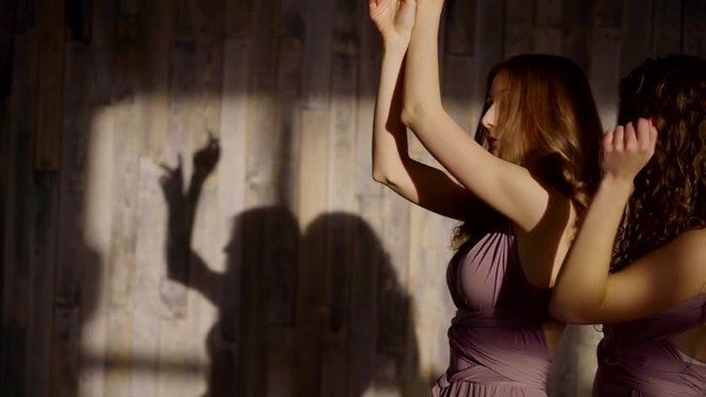 Two young sweet girls dancing indoor in lights of a winter sunset wearing soft puple dresses.