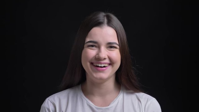 Portrait of young overweight brunette caucasian girl gets extremely happy smiling into camera on black background.