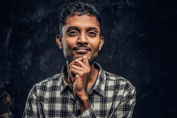 Fototapeta premium Close-up portrait of a handsome young Indian guy wearing a checkered shirt holding hand on chin and looking at a camera with a pensive look.