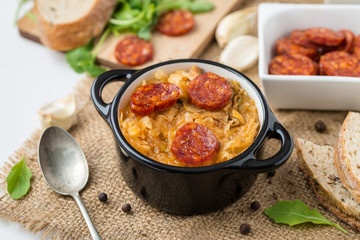 Slovak Christmas national cabbage soup in two small black pots with sausage on the jute background.