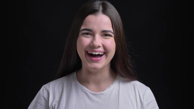 Portrait of young overweight brunette caucasian girl showing extreme happiness into camera on black background.