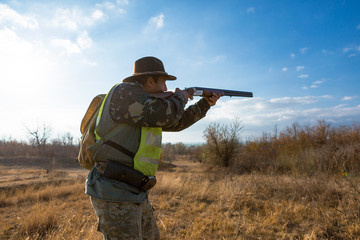 Silhouette of a hunter with a gun in the reeds against the sun, an ambush for ducks with dogs	