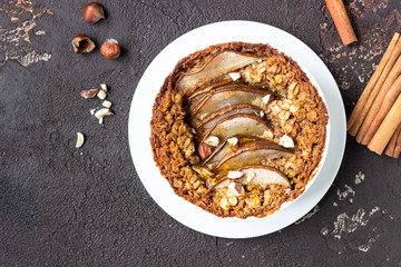 Diet crumble with oatmeal, cinnamon and pears decorated with hazelnut and honey in a frying pan for baking. Dark brown stone concrete. Top view, copy space.