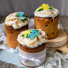 Three traditionally baked orthodox easter cakes with glace icing and bright blue and yellow flowers on woooden background with lace fabric. Easter kulich. Selective focus, copy space.