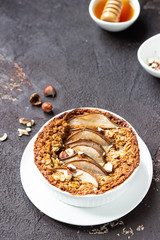 Diet crumble with oatmeal, cinnamon and pears decorated with hazelnut and honey in a frying pan for baking. Dark brown stone concrete. Top view, copy space.