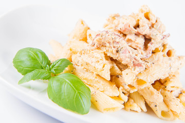 Pasta - penne with white cream sauce with bacon on a plate, decorated with fresh basil