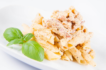 Pasta - penne with white cream sauce with bacon on a plate, decorated with fresh basil
