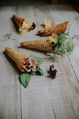 Waffle cones with bouquets of spring flowers and green herbs inside on a wooden rustic background. Soft selective lens focus.