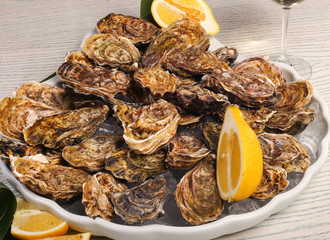 big plate of oysters with two lemons and vine on black wood background 