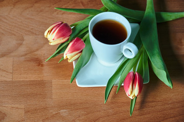 A bouquet of red tulips and a cup with black coffee on a wooden table.