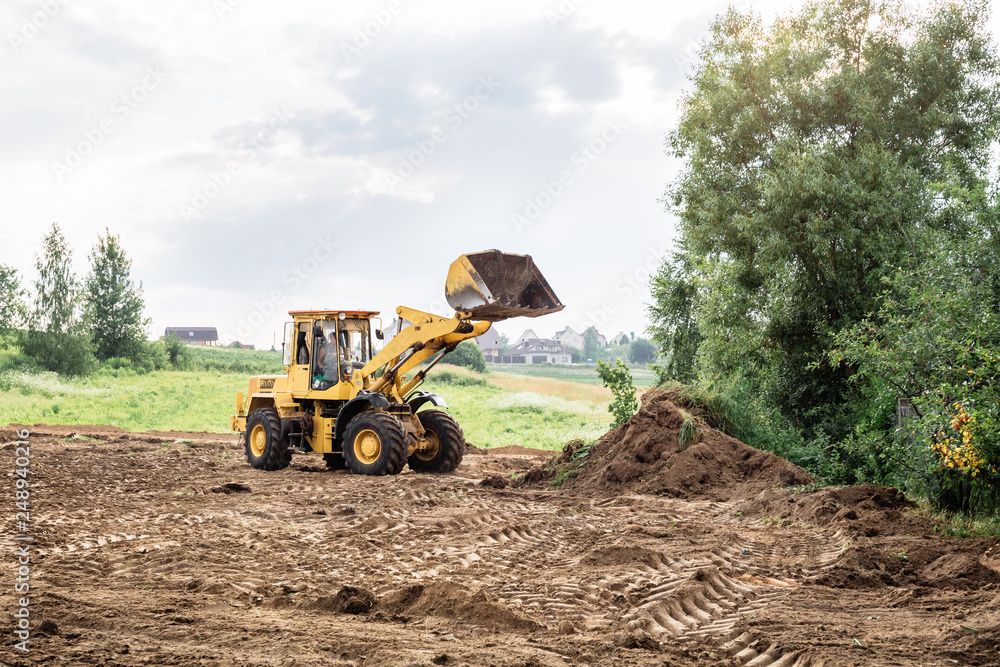 Wall mural large yellow wheel loader aligns a piece of land for a new building. May be cut to banner or wallpaper with copy space.