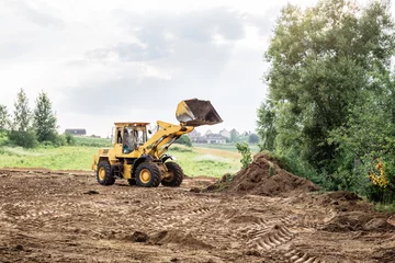 Fotobehang large yellow wheel loader aligns a piece of land for a new building. May be cut to banner or wallpaper with copy space. © Hanna