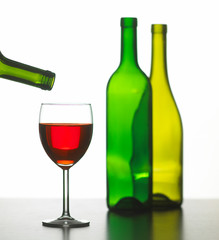 GLASS OF RED WINE WITH TWO GREEN WINE BOTTLES ON WHITE BACKGROUND