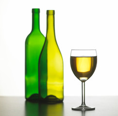 GLASS OF WHITE WINE WITH TWO GREEN WINE BOTTLES ON WHITE BACKGROUND