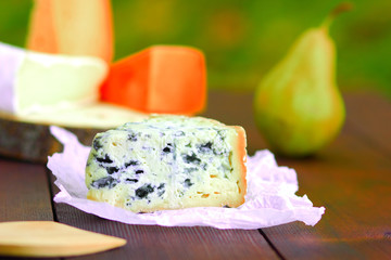 Various types of cheese and pear on wooden boards. Slices of cheese on blurred background. Dorblu, camembert and hard yellow cheese on parchment paper