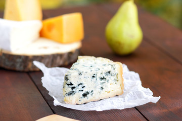 Various types of cheese and pear on wooden boards. Slices of cheese on blurred background. Dorblu, camembert and hard yellow cheese on parchment paper