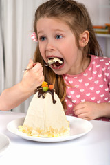 Studio shot of small  girl  sitting at a table and eating Easter cakes.