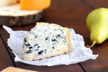 Various types of cheese and pear on wooden boards. Slices of cheese on blurred background. Dorblu,...