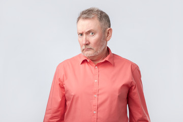 Fototapeta premium Senior man in red shirt frowning and squinting, showing disbelief or doubt