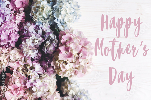 Happy Mother's Day text sign on beautiful hydrangea flowers on rustic white wood, flat lay. Colorful pink,blue,green,white border of hydrangea. Stylish floral greeting card.