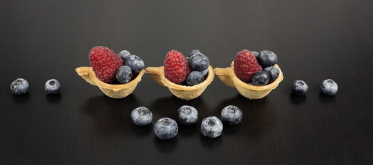 Fototapeta na wymiar Berry mix. Strawberries, blueberries and raspberries in tartlets in the form of a Cup on a black wooden background