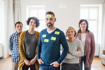 Young and old people standing with negative emotions adhesive notes during group therapy.