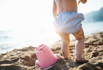 A midsection of small toddler girl with shorts playing on sand beach on holiday.